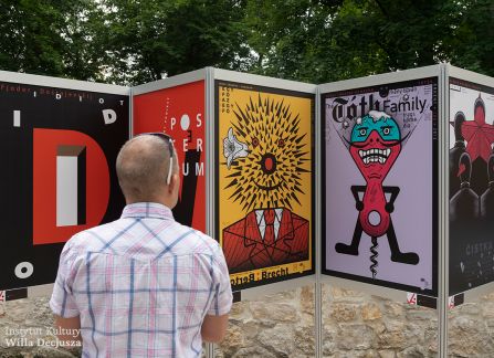 fotografia. art piknik w willi decjusza. plenerowa wystawa plakatów teatralnych. mężczyzna stoi przed ustawionymi w rzędzie plakatami.